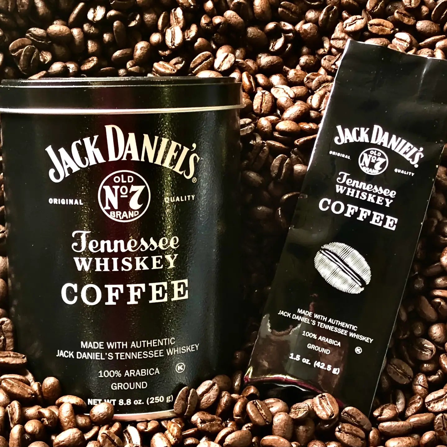 A black metal tin and matching black pouch of Jack Daniel's Tennessee Whiskey Coffee surrounded by scattered roasted coffee beans.