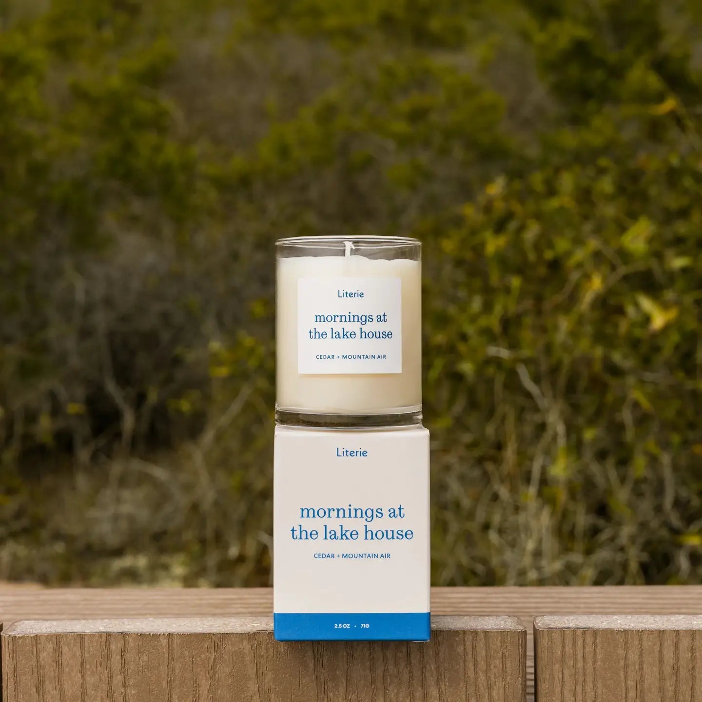 Candle and packaging labeled 'Mornings at the Lake House' on a wooden surface with a natural background.