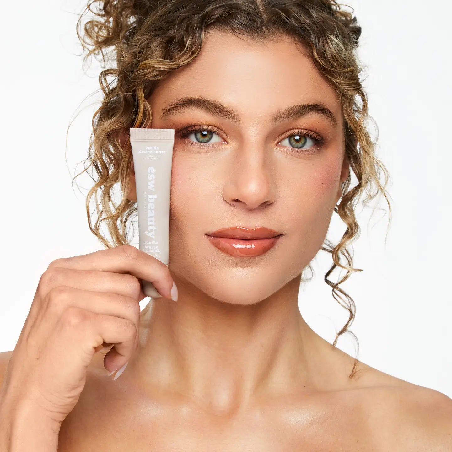 Woman holding a skincare product against a neutral background