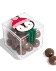 A clear acrylic cube container filled with chocolate-covered round candies, with a penguin illustration on the lid and two additional candies placed beside it on a white background.