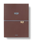 A brown textured hardcover notebook with a light blue elastic band and small gold charms, on a white background.
