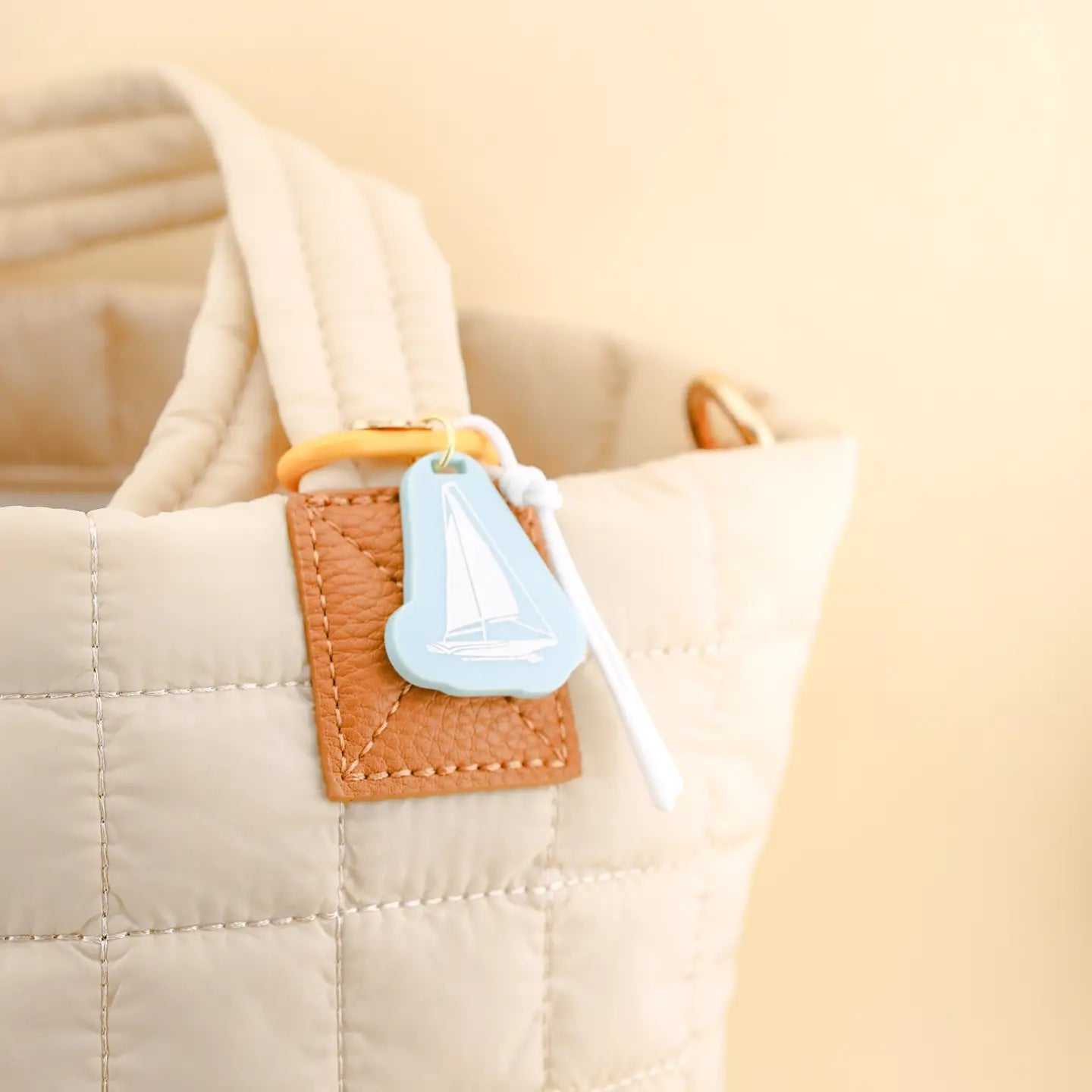 Close-up of a beige quilted bag with a brown leather patch and a blue tag.