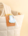 Close-up of a beige quilted bag with a brown leather patch and a blue tag.