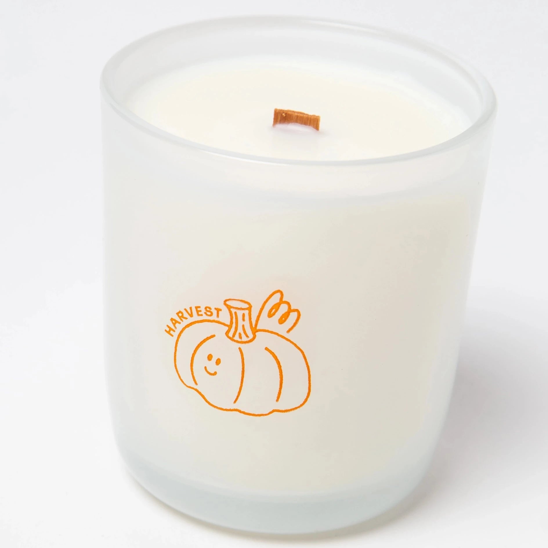 clear glass candle with an orange pumpkin that says "harvest" on it