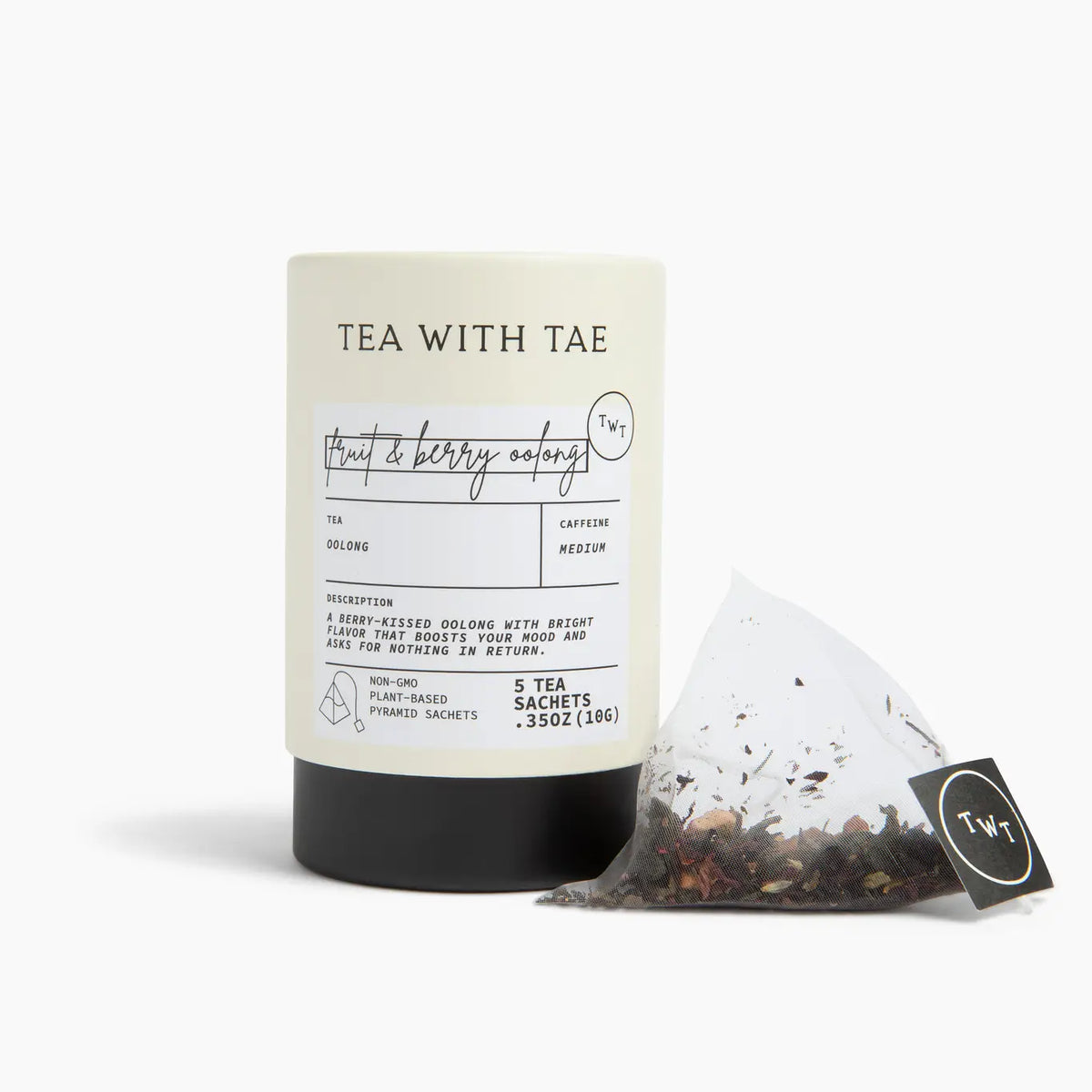 A tea product shot on a clean white background, featuring a cylindrical black canister with a cream label reading 'TEA WITH TAE' and a clear teabag with loose tea leaves and a black brand tag in front.