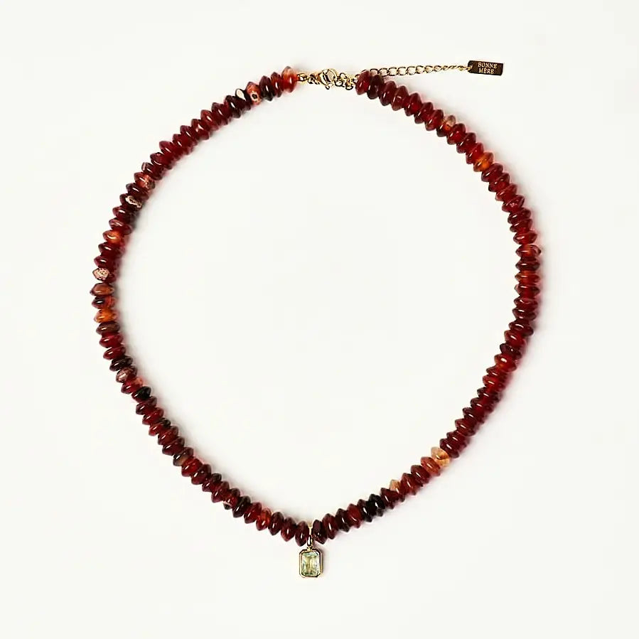 A beaded necklace made of faceted dark red and brown glass beads, featuring a small gold-toned pendant and an adjustable chain with a brand tag, displayed on a clean white background.