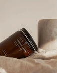 Brown candle jar labeled 'Oakmoss & Amber' on a textured surface with a neutral background