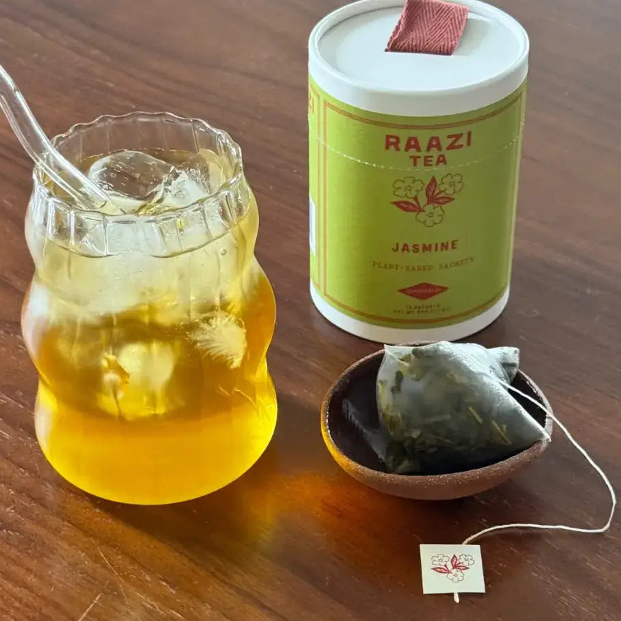 raazi jasmine green tea on a wood table next to a glass and sachet