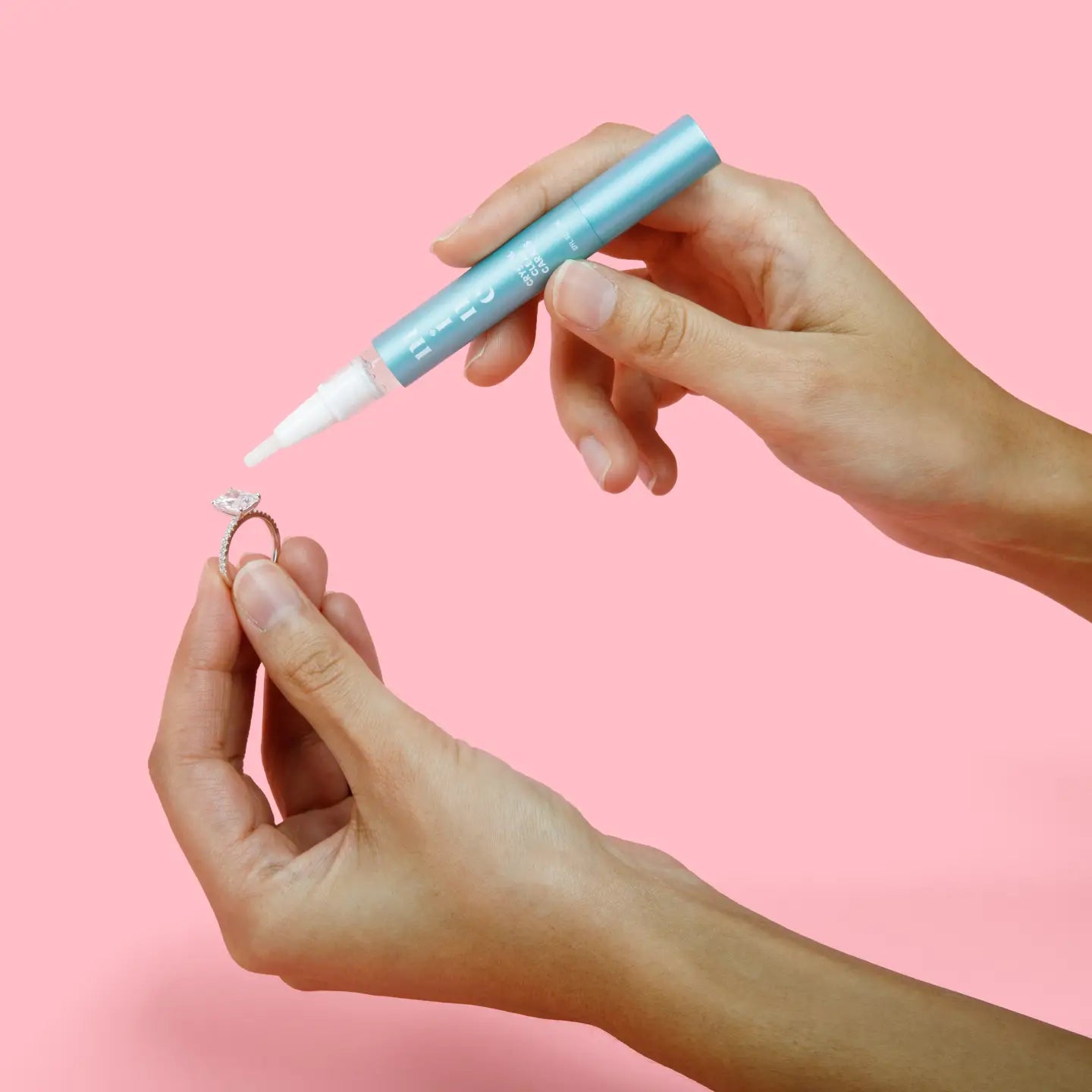 Person using a blue marker to write on a small object against a pink background