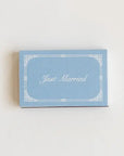 A small rectangular light blue card with a white decorative border and the words 'Just Married' in white script, placed on a plain off-white background.