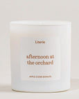 A white glass jar candle with a minimalist white label featuring the scent name 'afternoon at the orchard' in a warm brown font, with 'Literie' above and 'APPLE CIDER DONUTS' below, set against a clean off-white background.