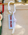 Keychain with 'Ski Bum' tag attached to a beige bag