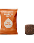 An orange bag of Tea Drops Pumpkin Spice naturally sweetened bagless black tea, shown next to a single square brown tea drop on a plain white background.