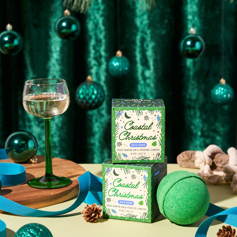 Coastal Christmas bath bombs and packaging on a festive table with a glass of wine and decorative items.