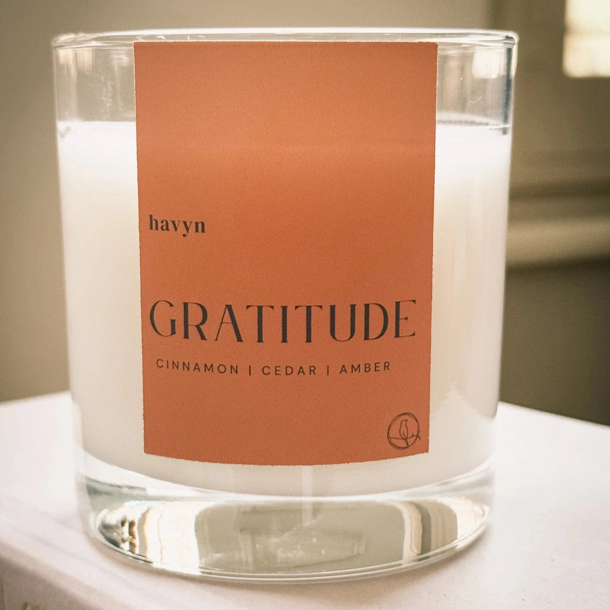 candle from the Havyn brand, labeled "Gratitude." This candle has fragrance notes of cinnamon, cedar, and amber, evoking a warm and cozy atmosphere. close-up of the product, showcasing it on a minimal surface, emphasizing the elegant simplicity of the packaging.