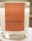 candle from the Havyn brand, labeled "Gratitude." This candle has fragrance notes of cinnamon, cedar, and amber, evoking a warm and cozy atmosphere. close-up of the product, showcasing it on a minimal surface, emphasizing the elegant simplicity of the packaging.