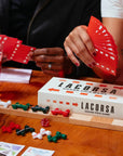 Two people playing a Lacorsa Grand Prix Game with cards and game pieces on a wooden table.