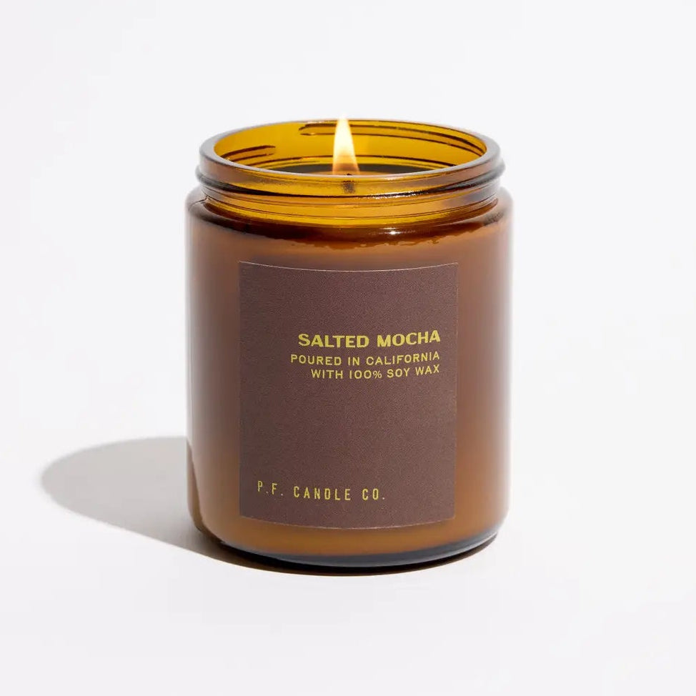 An amber glass jar candle with a lit flame, featuring a dark brown label that reads 'SALTED MOCHA' and 'P.F.