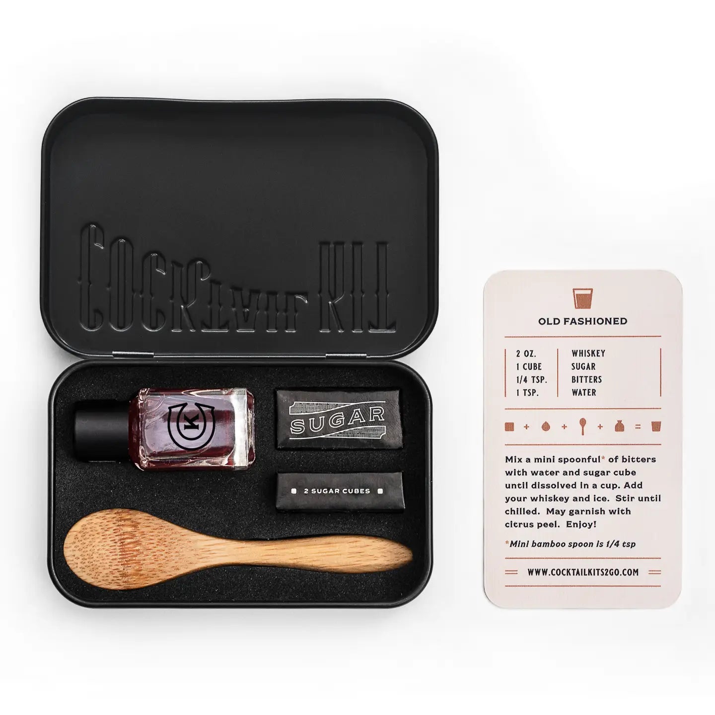 Cocktail kit with black tin, cocktail ingredients, and wooden spoon on a white background