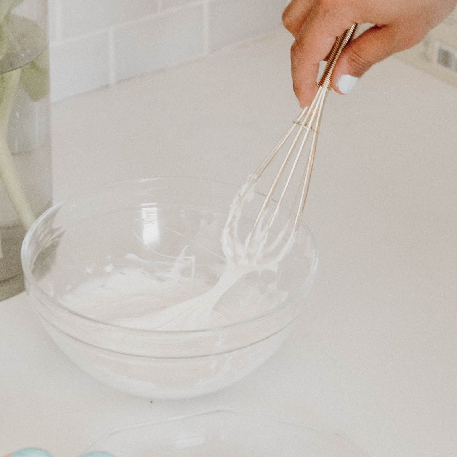 Gold whisk mixing frosting in a glass bowl