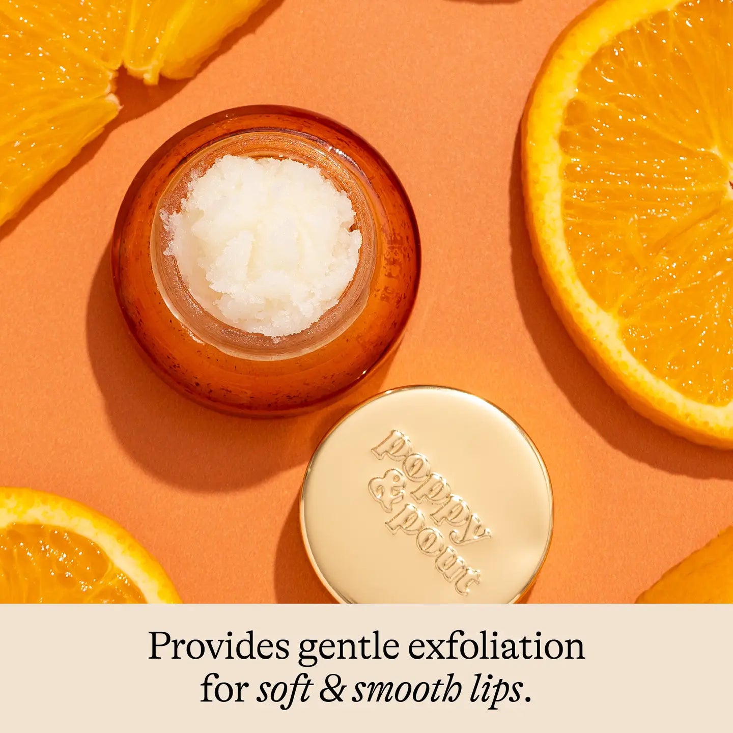 Small jar of lip scrub with a gold lid on an orange background with sliced oranges.