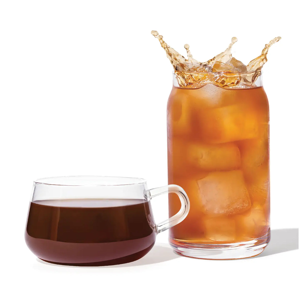 Glass of iced coffee with splashing liquid next to a cup of black coffee on a white background