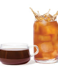 Glass of iced coffee with splashing liquid next to a cup of black coffee on a white background