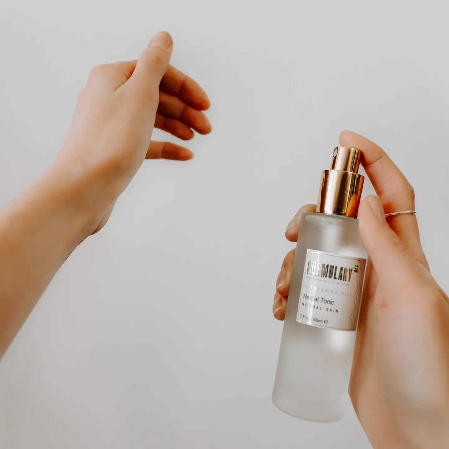 Person holding a perfume bottle with a gold cap against a plain background