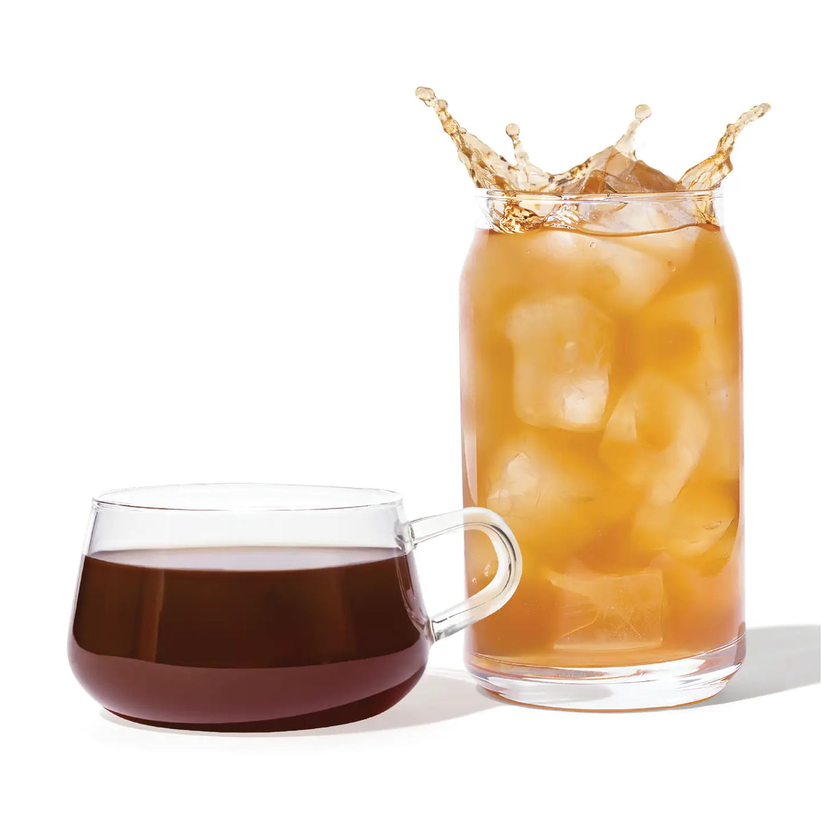Glass of iced coffee with a splash next to a cup of black coffee on a white background