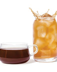 Glass of iced coffee with a splash next to a cup of black coffee on a white background