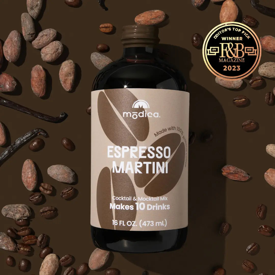 Bottle of Modica Espresso Martini mix surrounded by coffee beans and vanilla beans on a brown background.