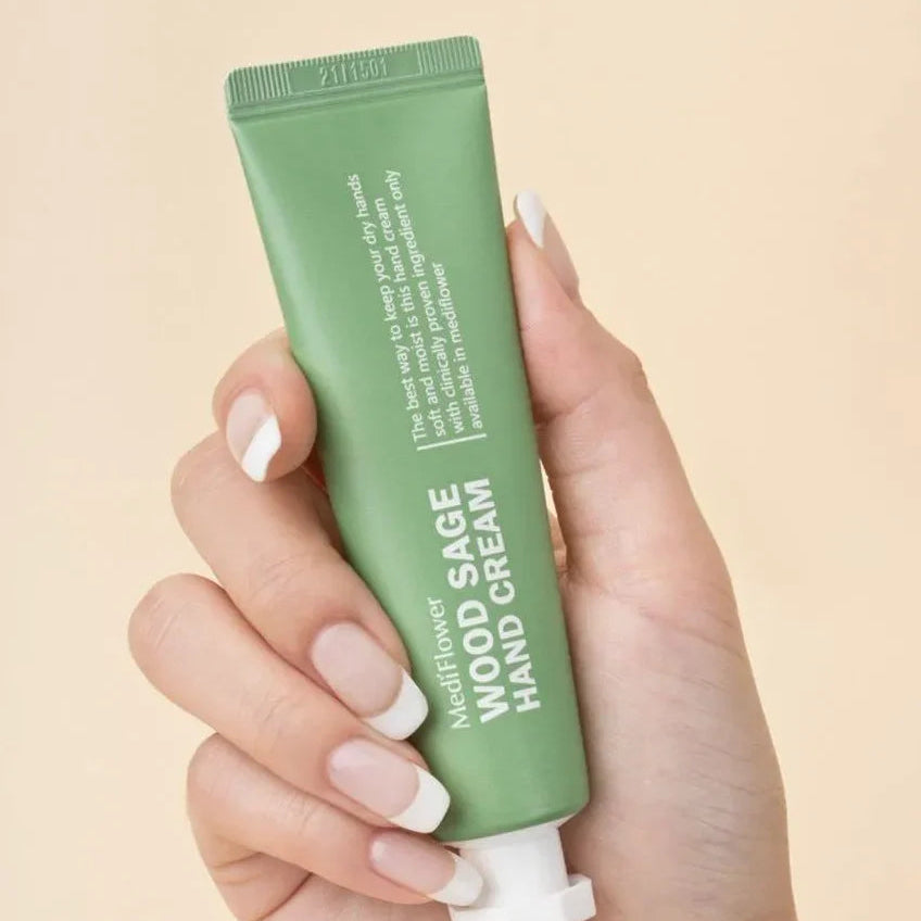 Hand holding a green tube of hand cream against a beige background