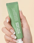 Hand holding a green tube of hand cream against a beige background