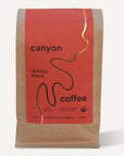 A package of Canyon Coffee's Holiday Blend featuring a minimalist red and kraft paper design with a gold wavy line on the label. The text highlights it as a "12oz" filter coffee roasted in Los Angeles.