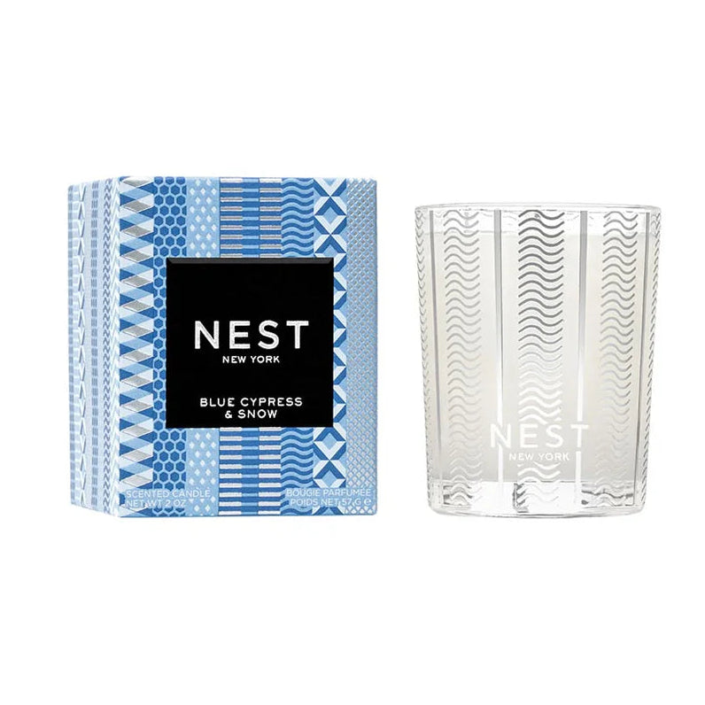 box with blue and white designs and a black label with white writing that says "blue cypress and snow" next to a white candle