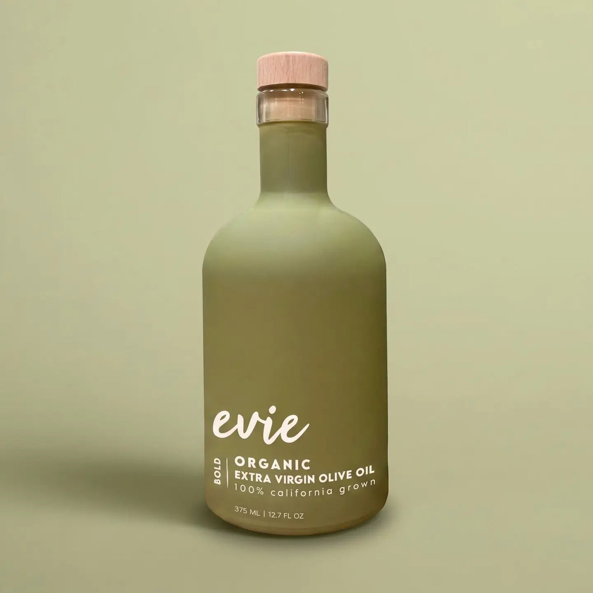 A frosted olive green glass bottle of Evie Bold Organic Extra Virgin Olive Oil with a light pink cap, set against a solid sage green background.