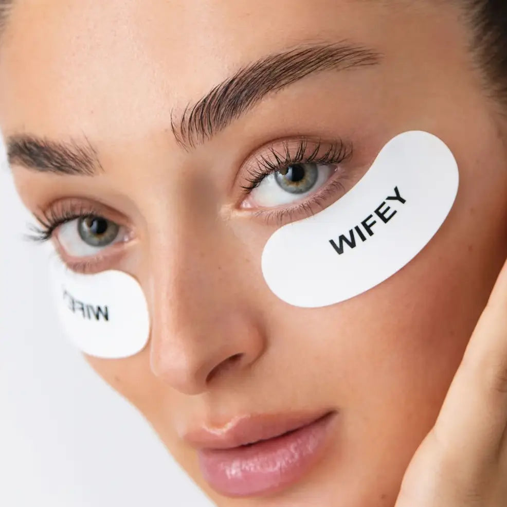 Close-up of a person wearing eye patches with 'WIFEY' text on a neutral background