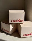 Three 'scandles' boxes stacked against a neutral wall.