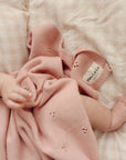 Baby wearing pink knitted booties and holding a pink blanket on a soft surface