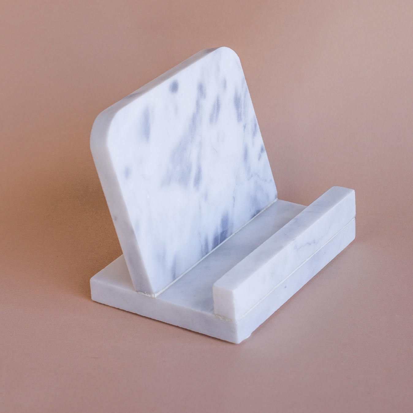 A white marble cookbook stand photographed in front of a mocha brown background.