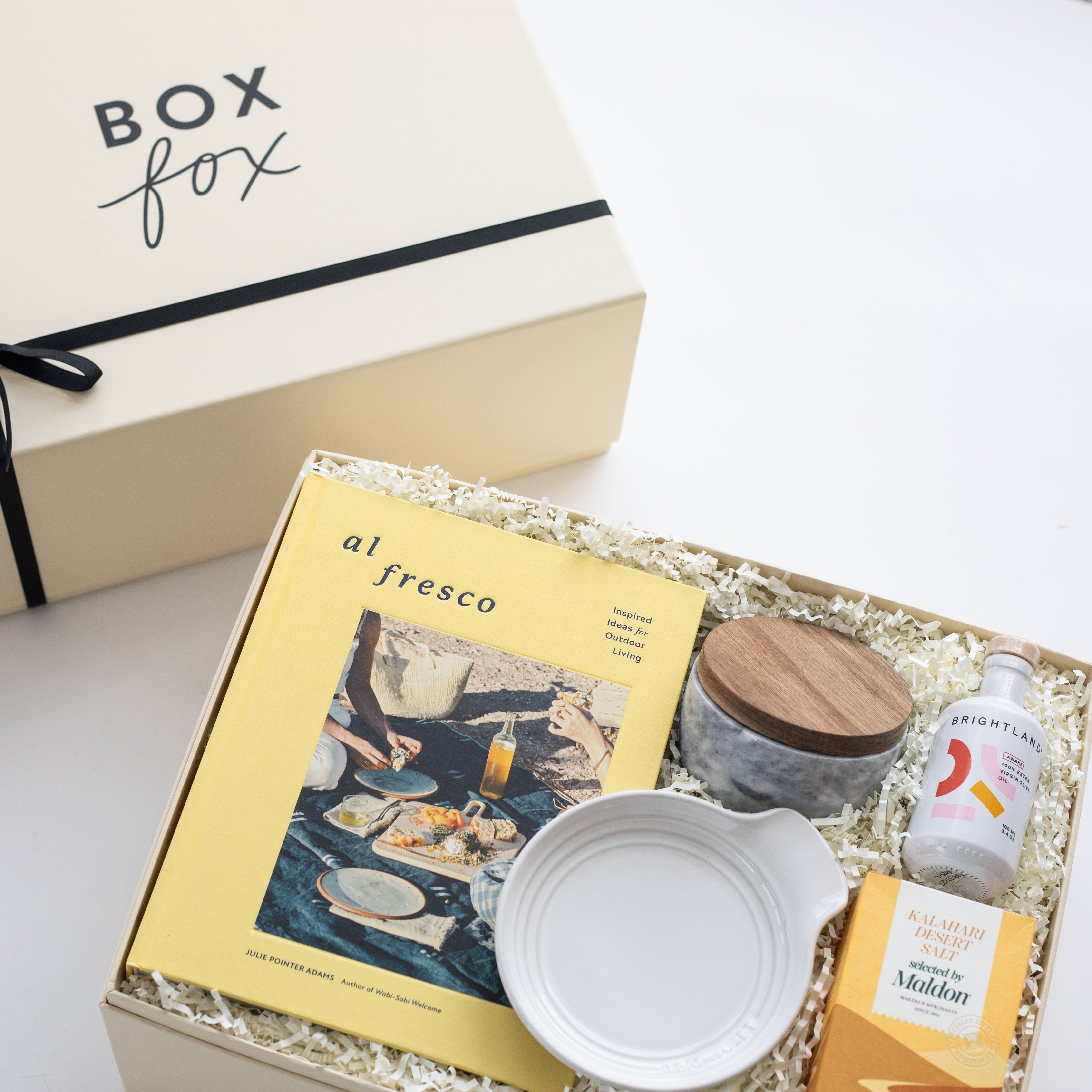 Gift box with 'Box Fox' branding, containing a book, bowl, and other items on a light background.