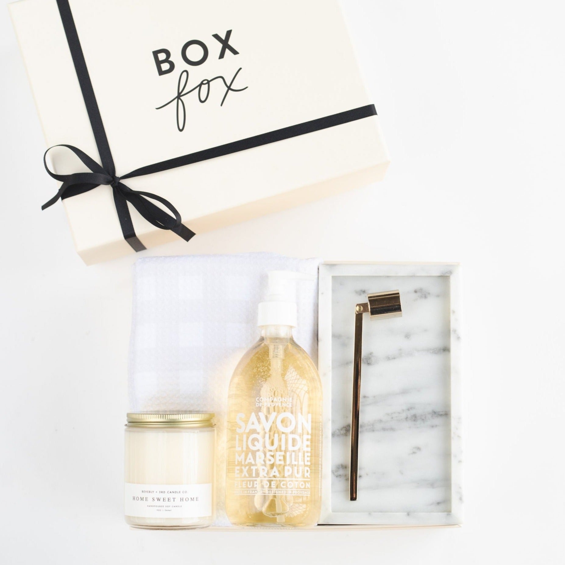 BOXFOX Original creme Housewarming Gift Box packed with Geometry Linen Plaid Tea Towel, Mielle Marble Tray, Vivie Gold Candle Snuffer, Beverly + 3rd Home Sweet Home Candle, and Compagnie de Provence 16.7 oz Liquid Hand Soap.