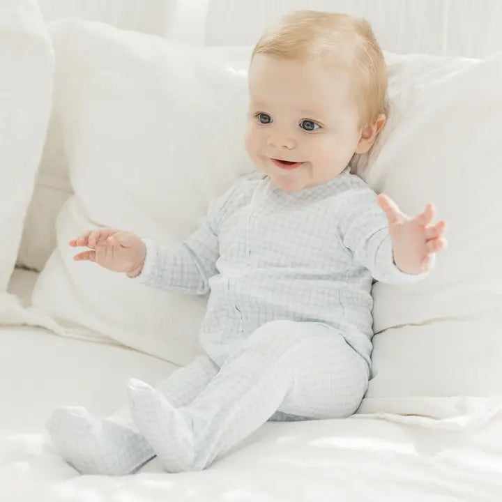 Baby in a light gray outfit sitting on a white surface