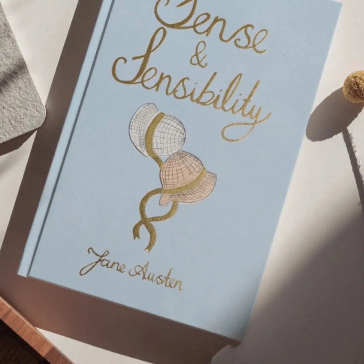 Book cover of 'Sense & Sensibility' by Jane Austen with a bonnet illustration on a light blue background.