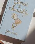 Book cover of 'Sense & Sensibility' by Jane Austen with a bonnet illustration on a light blue background.