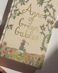 Book cover of 'Anne of Green Gables' with a illustration of a girl in a field.