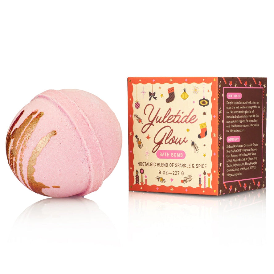 Pink bath bomb with gold glitter next to its packaging on a white background
