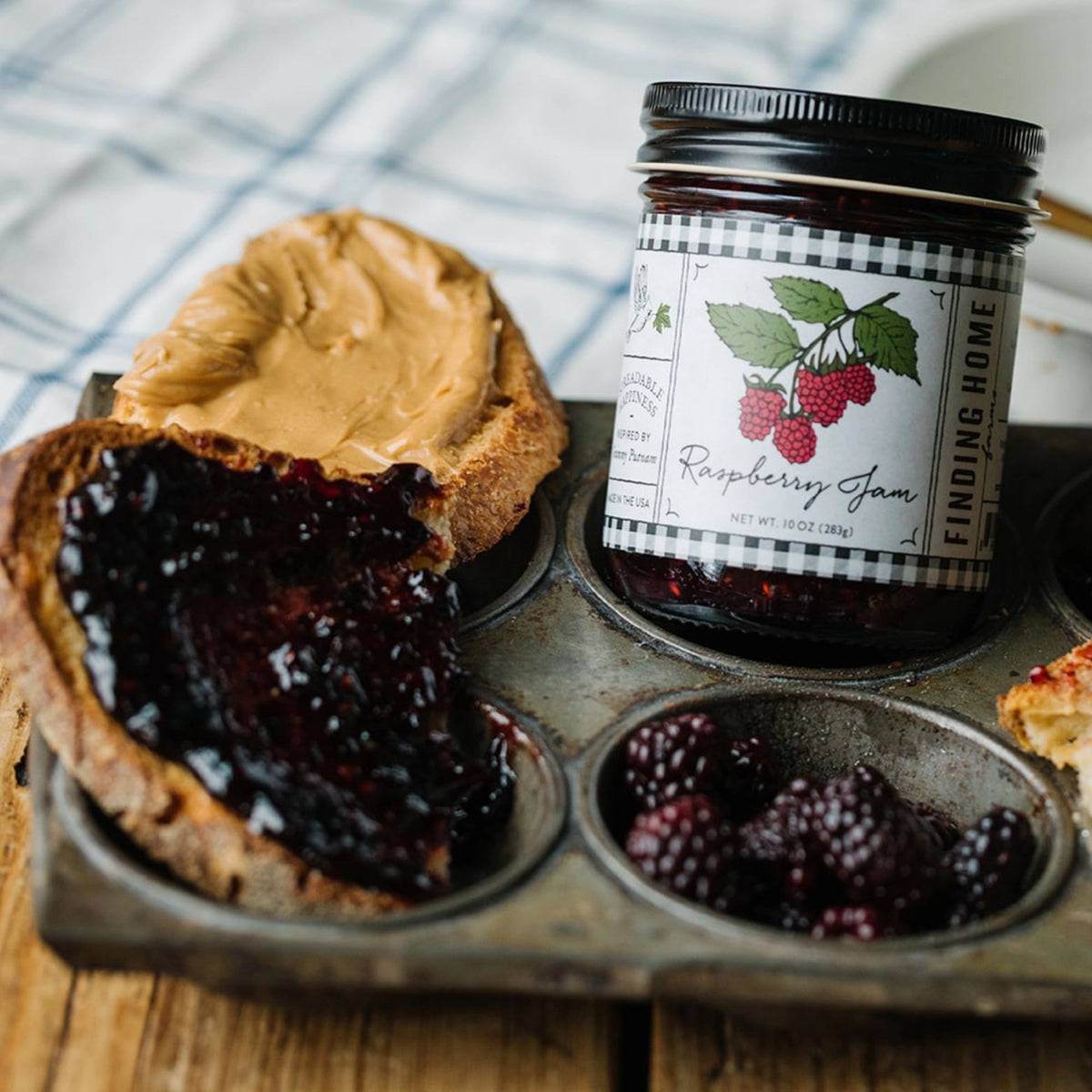 Jar of raspberry jam with a muffin and peanut butter on a wooden surface