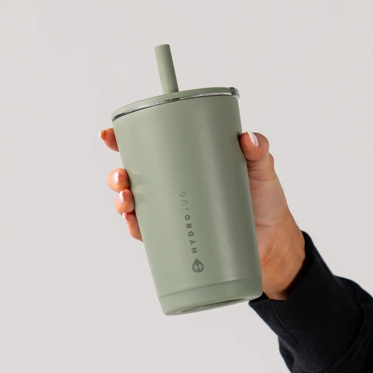 Hand holding a green Hydroflask tumbler with straw on a light gray background
