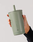 Hand holding a green Hydroflask tumbler with straw on a light gray background